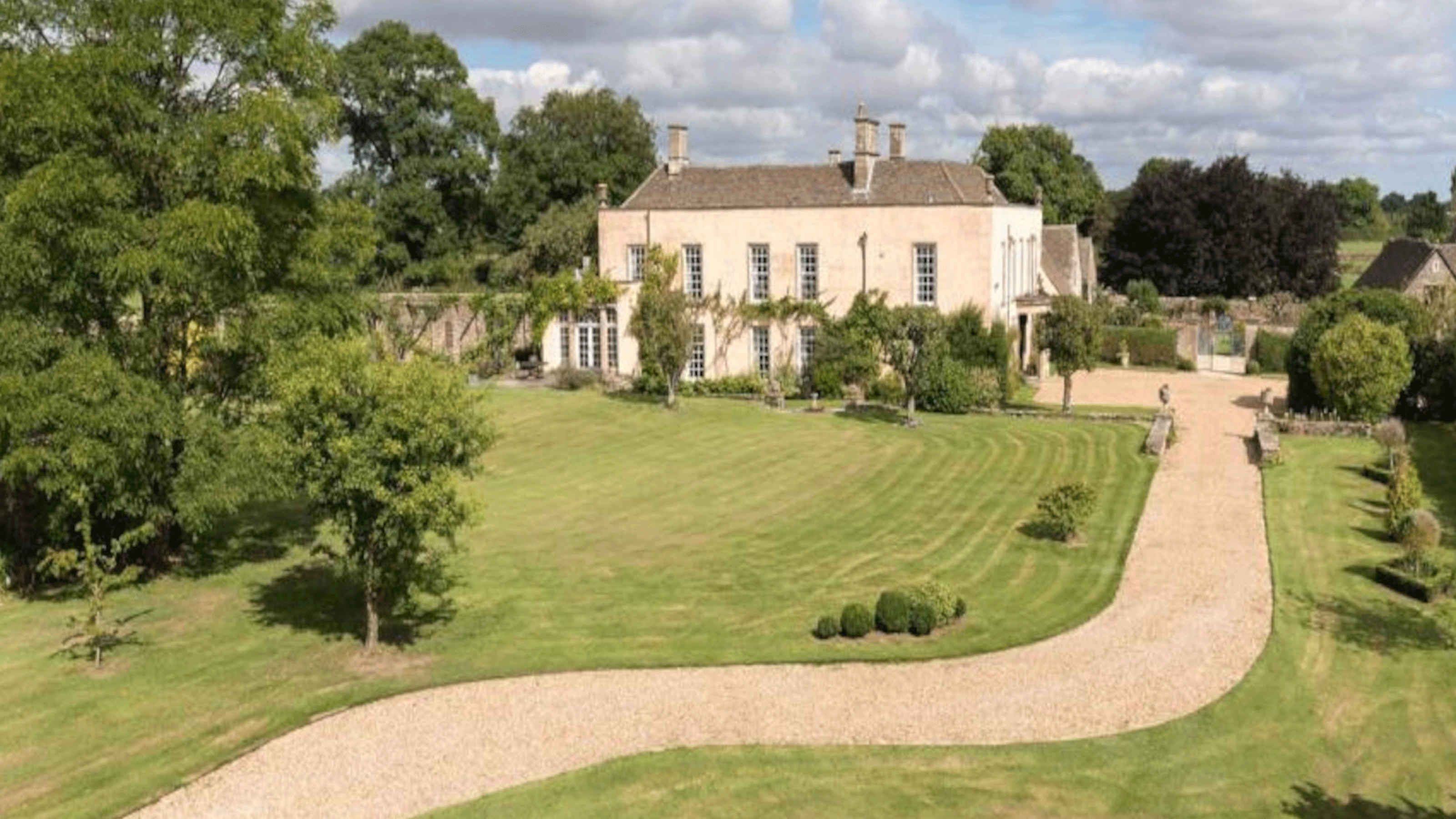 country house sits at the end of gravel path flanked by green grass and trees