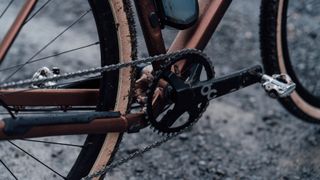 A 3/4 shot of the single front chainring of a copper coloured bike, with mud splattered on it
