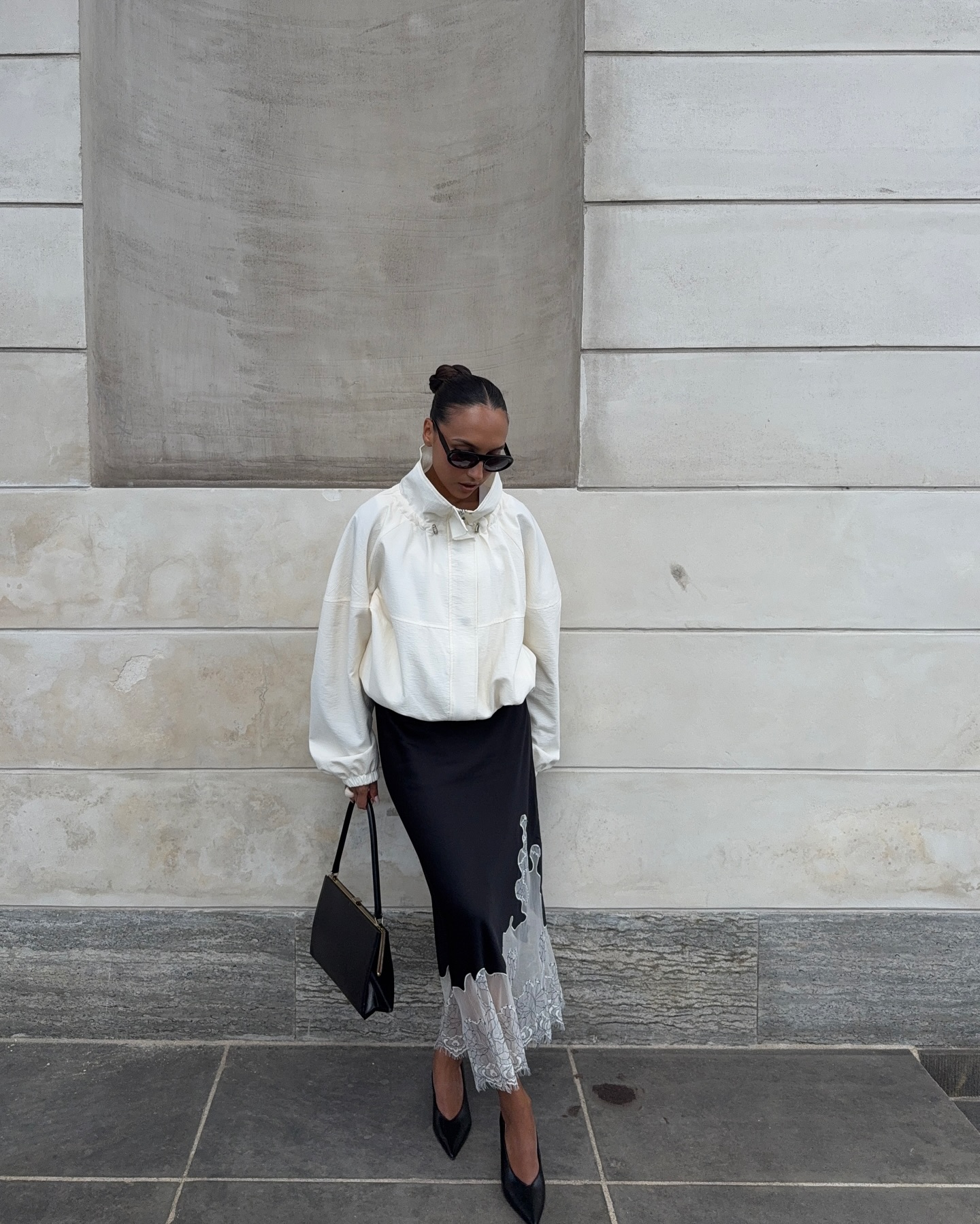 An image of an influencer wearing a white windbreaker, black skirt with white lace trim and black heels in Copenhagen.
