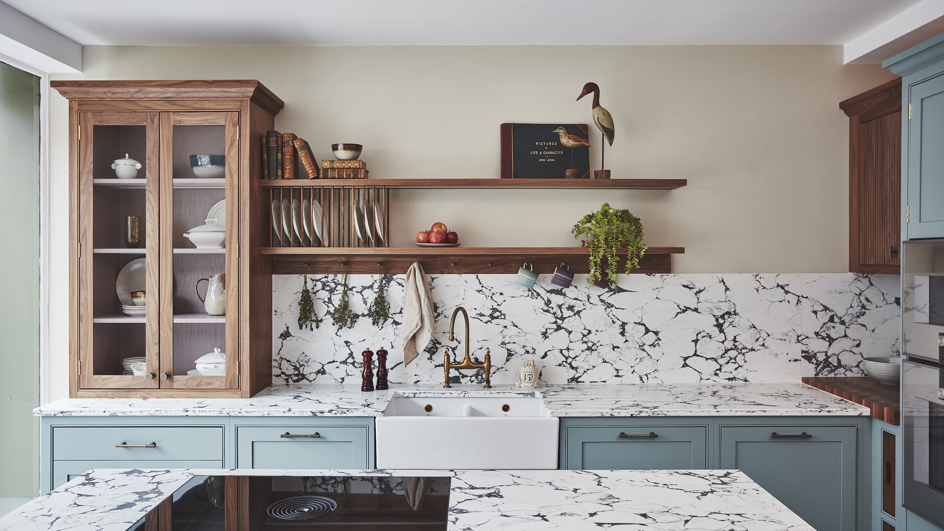 blue and wood kitchen with marble worktops and an open shelf above the countertop as well as a large glass fronted cabinet on the left side of the kitchen 