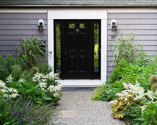 A front yard with symmetrical planting on sides, gravel path, and black front door