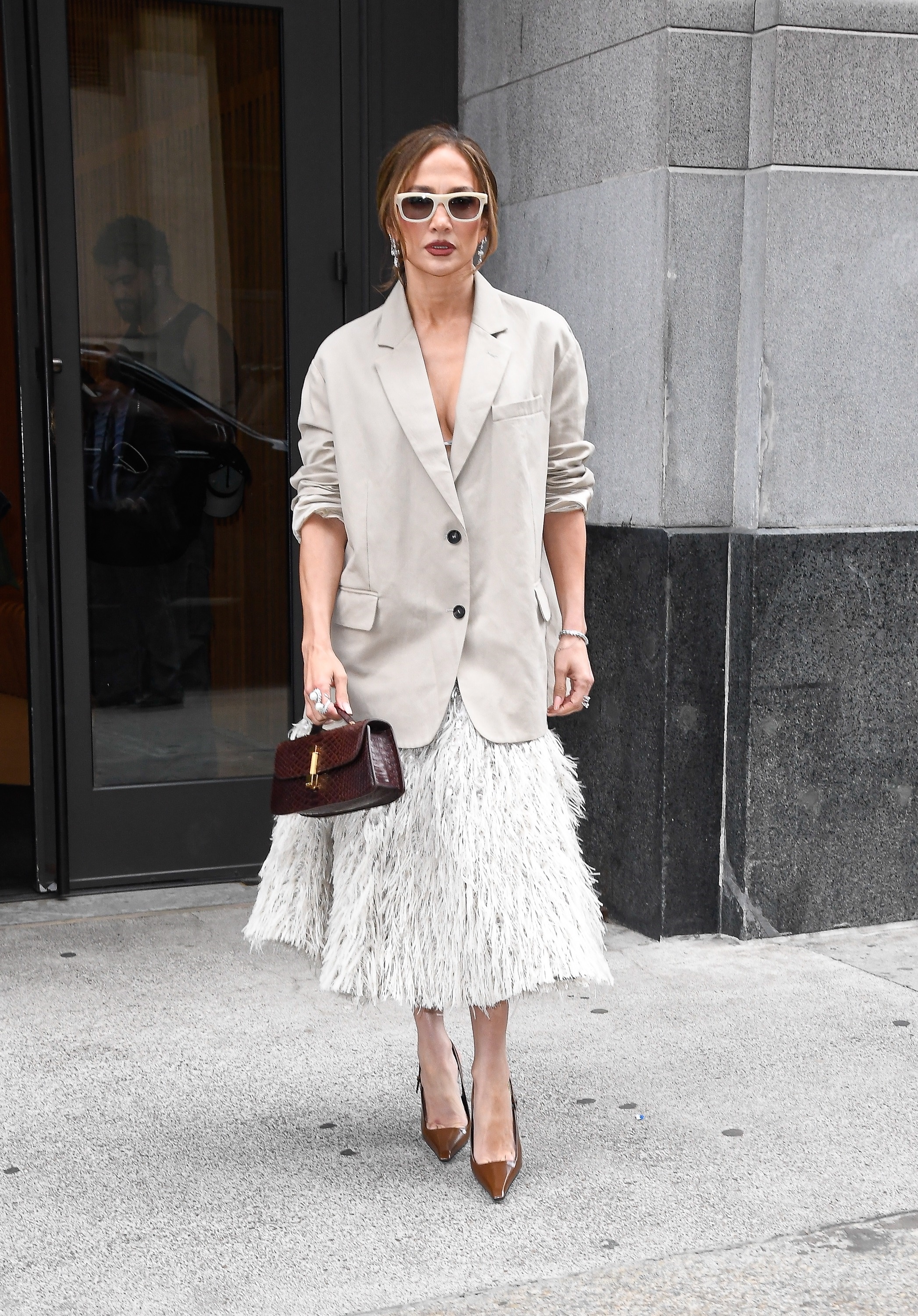 Jennifer Lopez wears a beige single breasted blazer with a textured skirt and brown glossy heels.