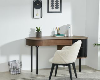 Zaragoza Desk in walnut in the corner of a white room with white boucle chair, plants and white and black rug on the floor