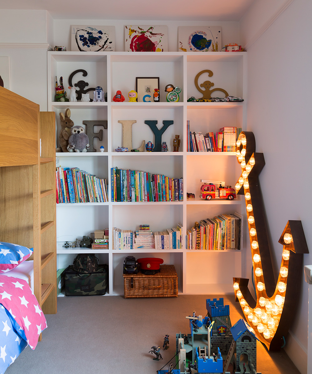 Small bedroom ideas for kids with built-in white storage, a wooden bunk bed and statement anchor neon lighting.