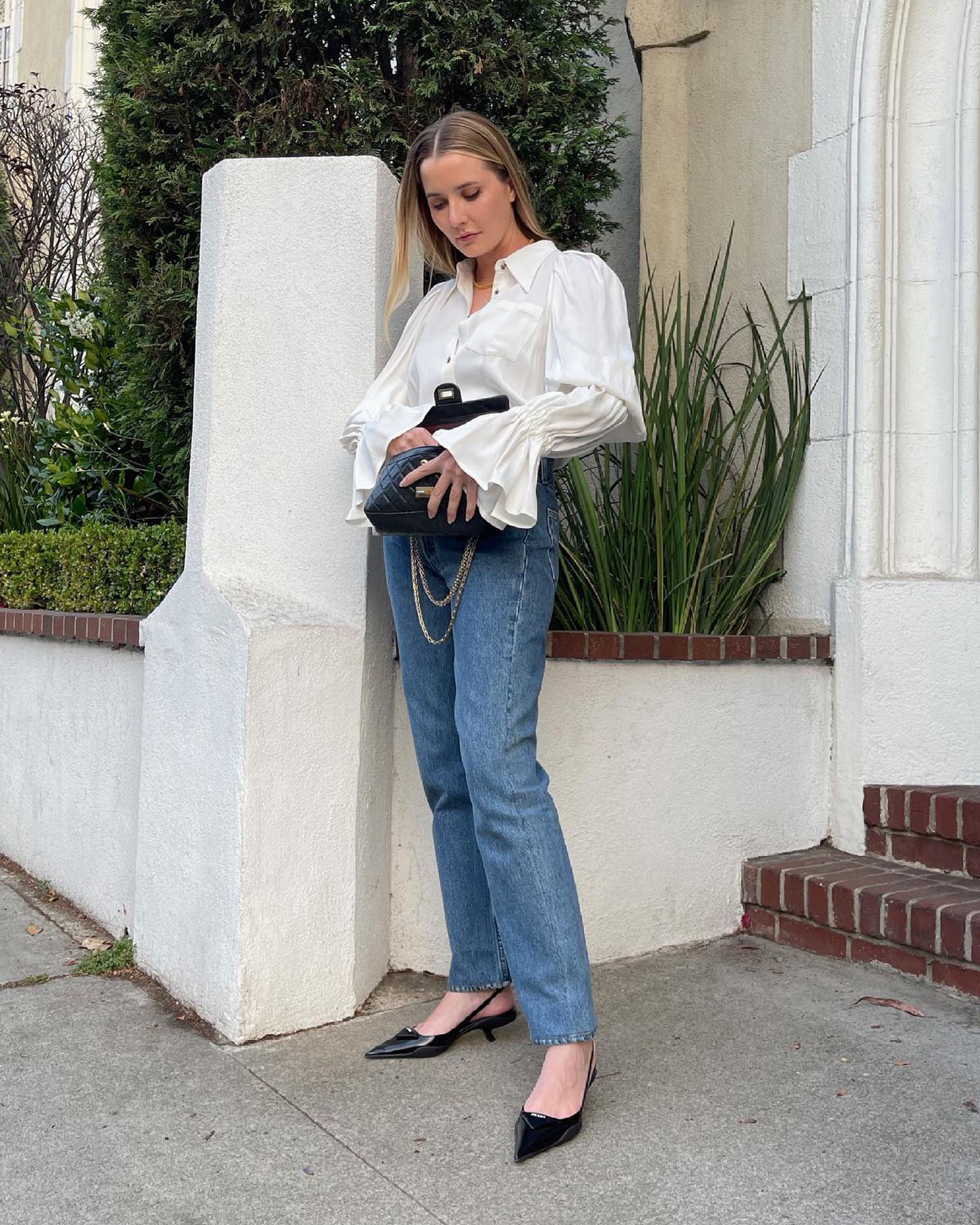 fashion editor Kristen Nichols poses in an outfit with statement white top, jeans, and black slingback kitten heels
