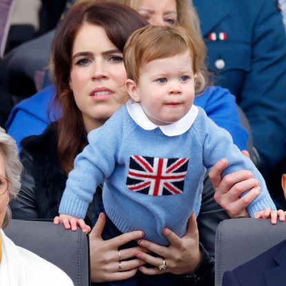 Princess Eugenie holds her son August who wears a light blue sweater with a Union Jack flag on it, and Prince George wears a navy suit with a blue tie