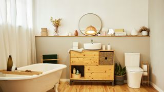 modern rustic bathroom with freestanding bath, wooden cabinets, floating wood shelving and a round mirror
