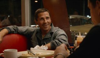 Ford V. Ferrari Christian Bale smiles in front of a cluttered diner table
