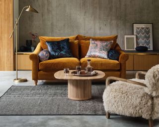 Heals orange velvet sofa in front of concrete wall on polished concrete flooring with furry chair