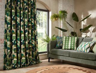 living room with green retro drapes, green stripe sofa, green printed cushions, plants, exposed painted brick wall, natural rug