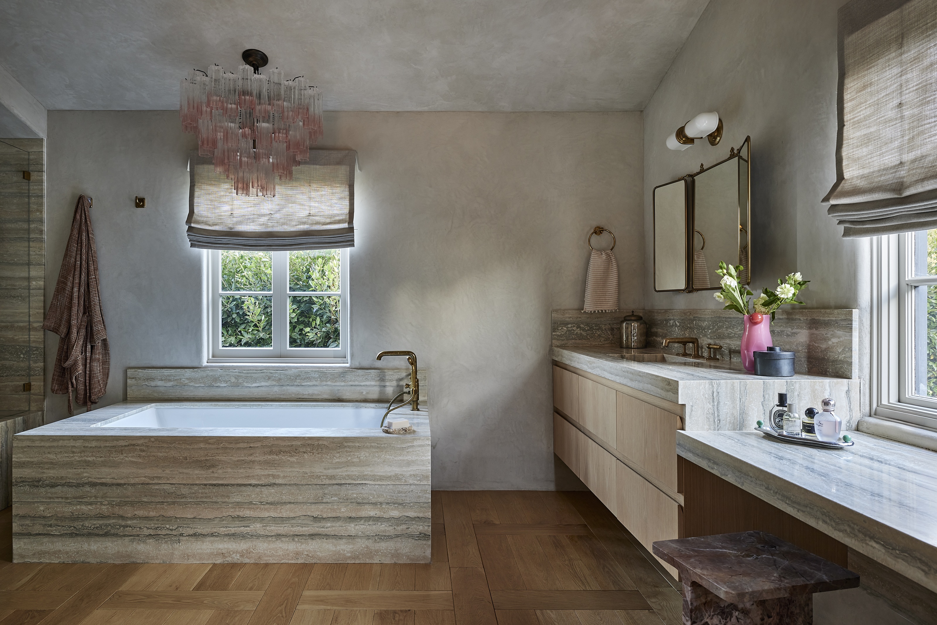 a limewash bathroom with a stone bath and vanity, and a murano glass pink chandelier