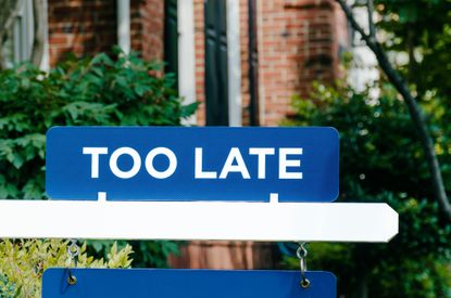 A real estate sign in front of a house reading "too late."