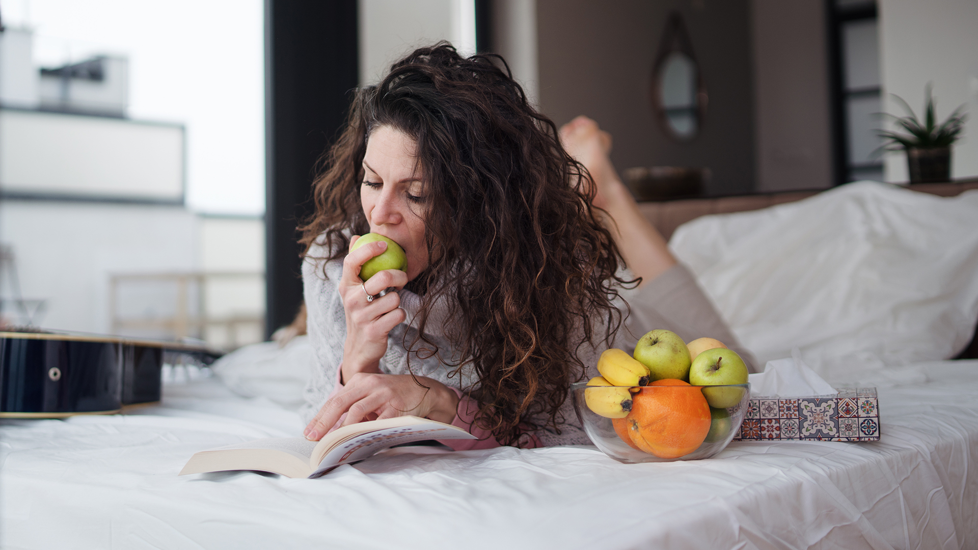Woman lying on bed and eating fruit