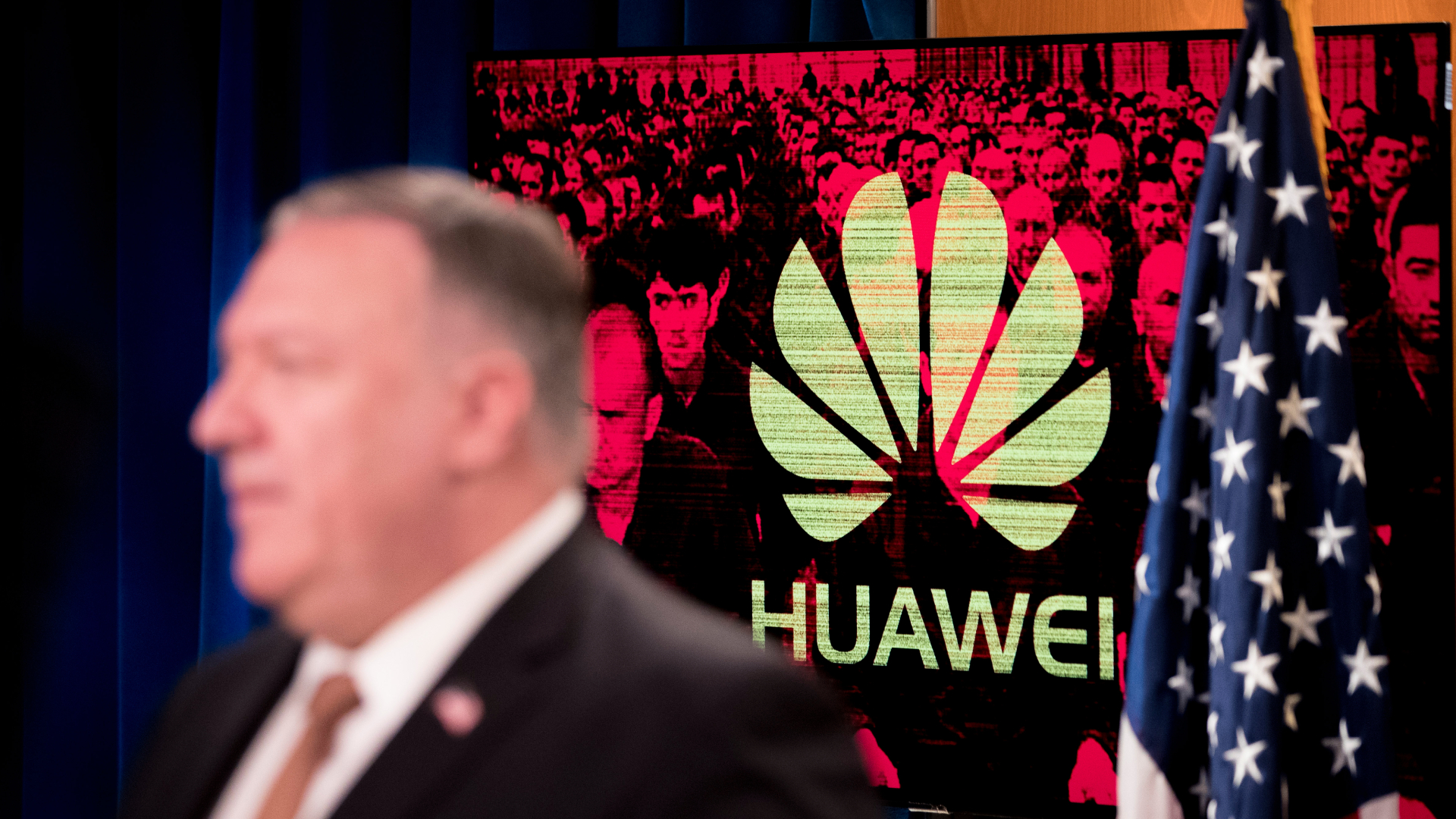 A monitor displays the logo for Huawei behind Mike Pompeo