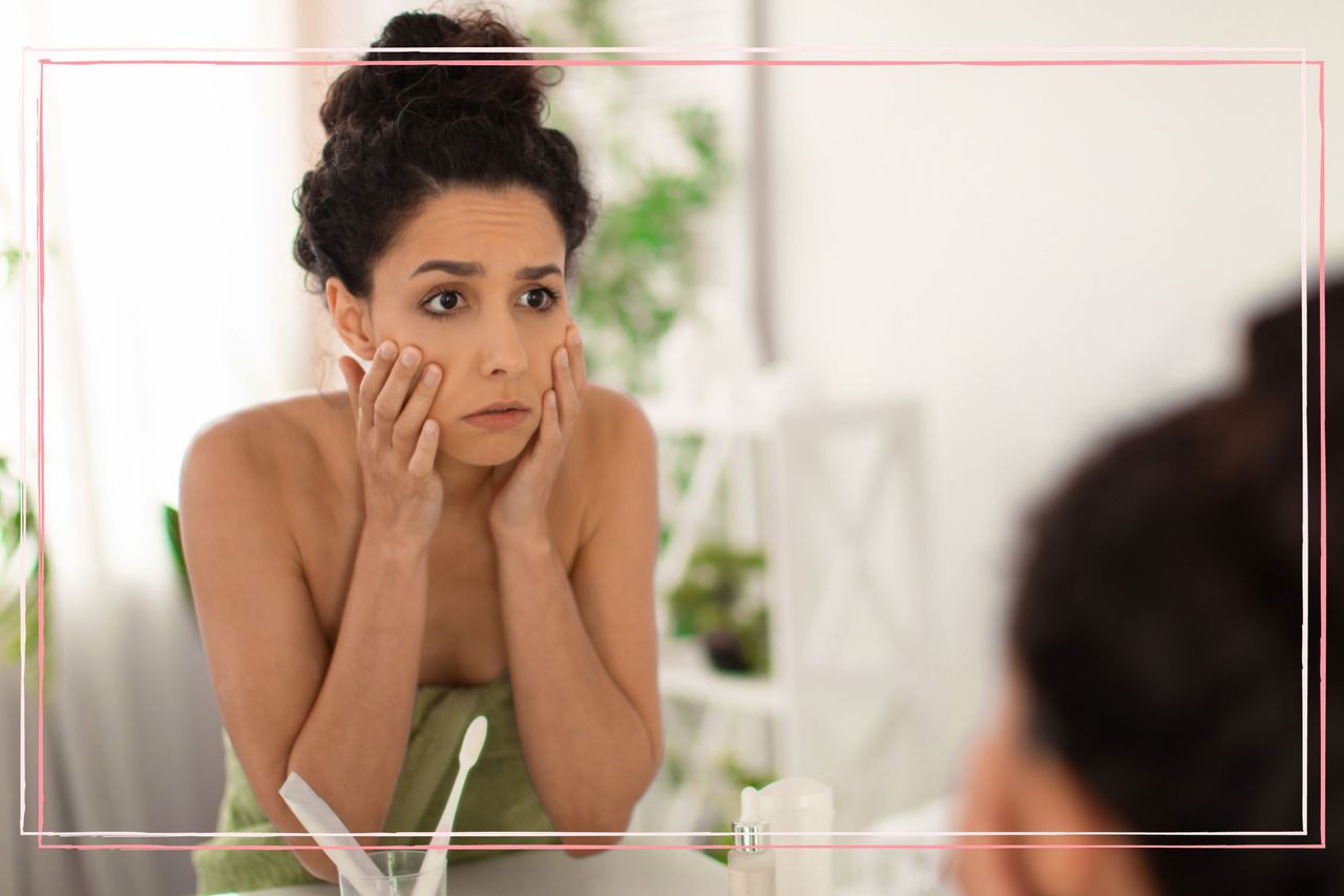 An upset looking woman looking at her face in the mirror