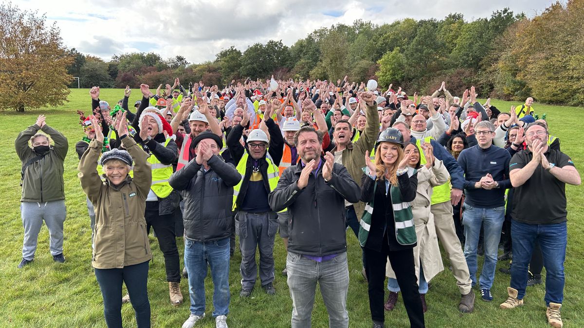 Gillian Wright, Perry Fenwick, Nick Knowles, Scott Maslen, Gaby Blackman and Zaraah Abrahams stand in a field with many volunteers who have taken part in DIY SOS: EastEnders 