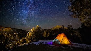 A tent with a light shining from the inside under the stars