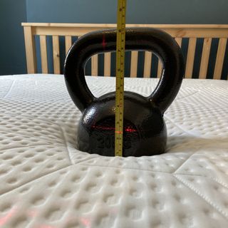 Black kettle bell on a white mattress with a wooden bed frame and a measuring tape