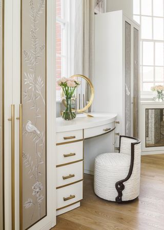 white fitted vanity between two closets. White with gold fixture, vase of roses and gold mirror, chinoiserie on closet doors