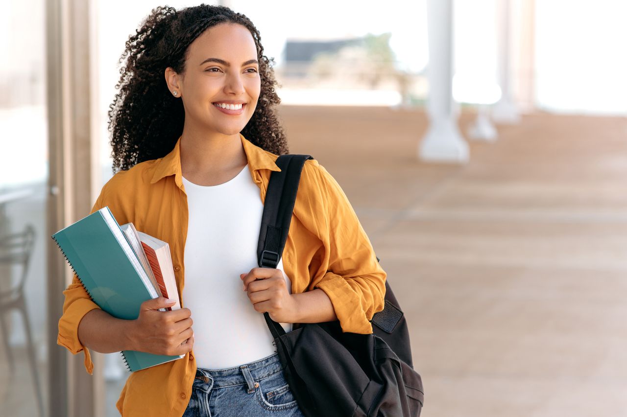 A happy student with a backpack and holding books.