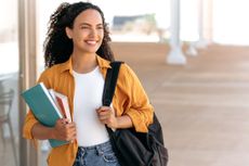 A happy student with a backpack and holding books.