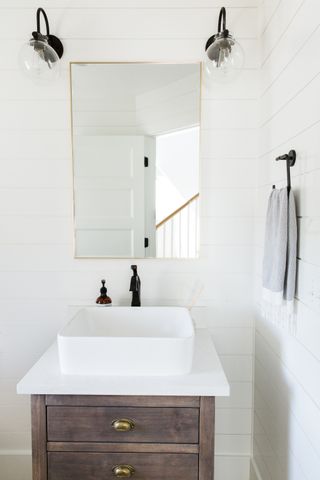 white painted bathroom with white shiplap walls black fixtures and fittings and brass mirror