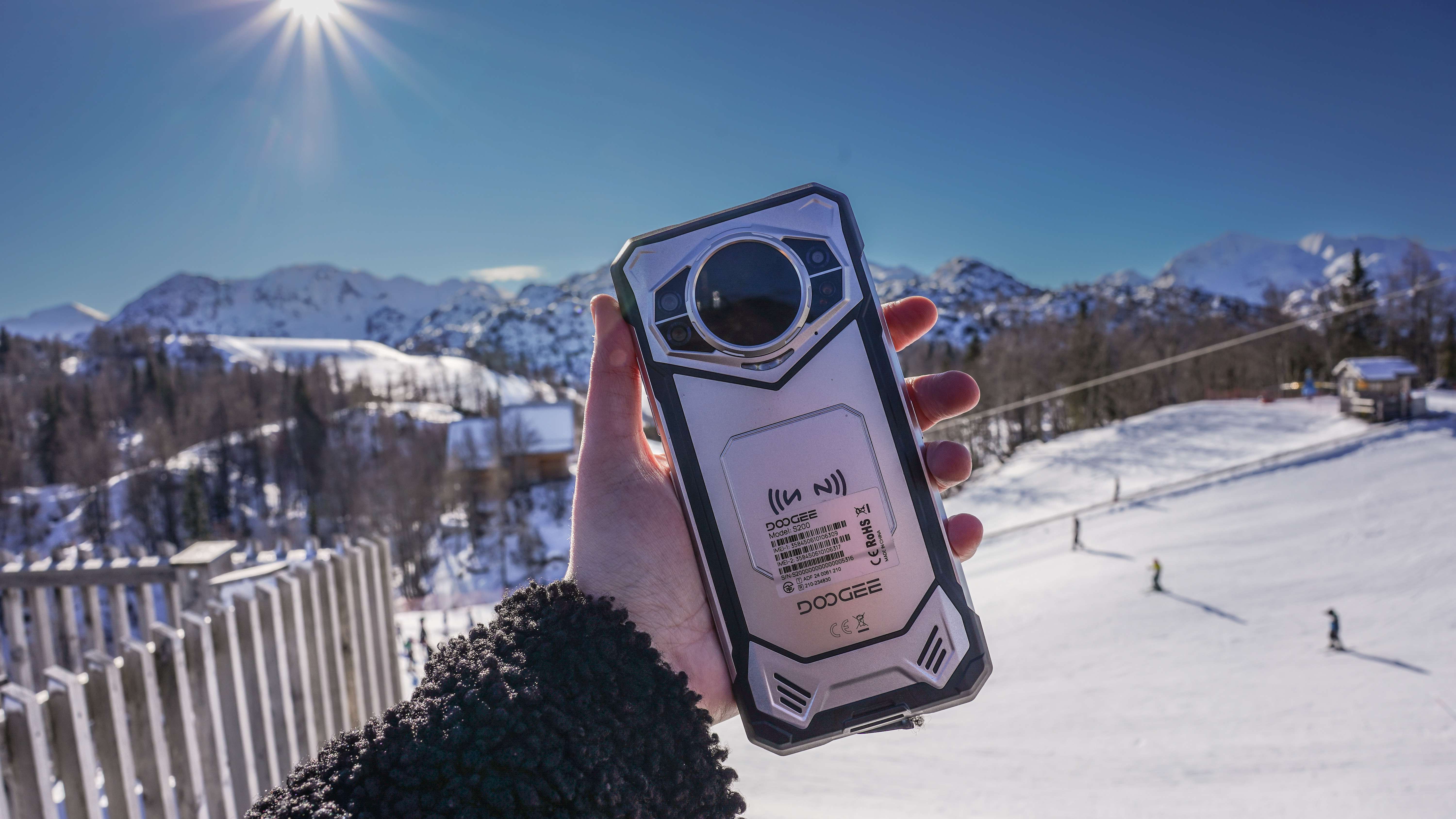 Doogee S200 rugged phone being held in hand with ski resort in background