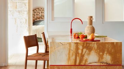 a warm tone marble island with a bright red faucet