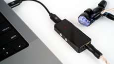 Promotional photo of the Campfire Audio Relay DAC next to a pair of in-ear monitors, plugged into a laptop