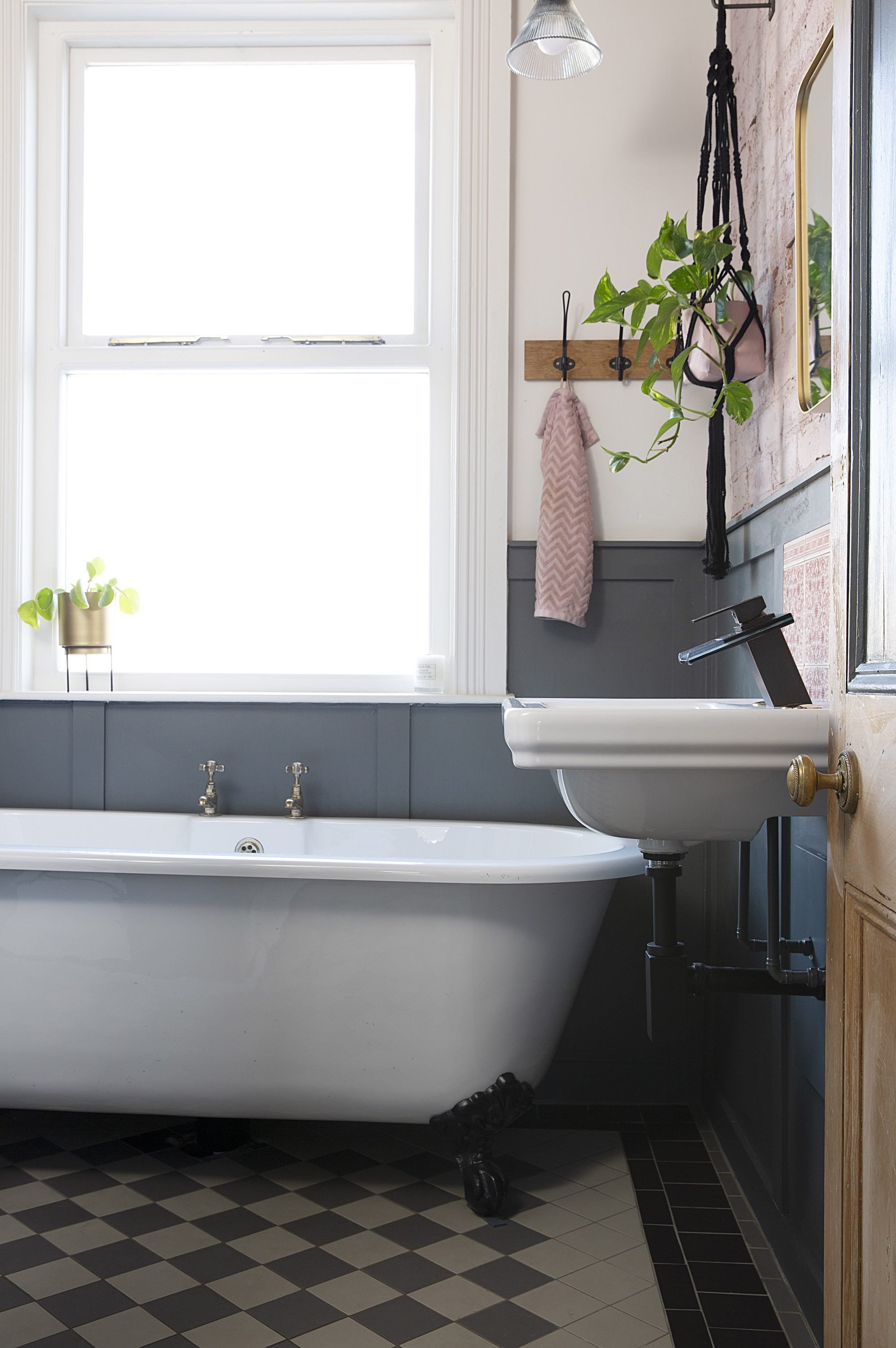 bathroom with a roll top bath, patterned monochrome flooring, grey paneling and an exposed brick walll