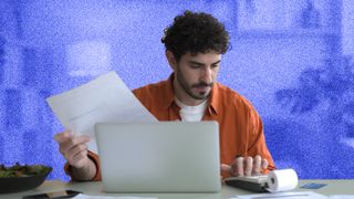 Front view of a young man checking bills in his apartment.
