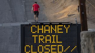 A walker passes a trail closure sign during CA wildfires