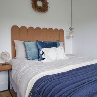 white bedroom with boucle headboard blue throw white bedding pendant light