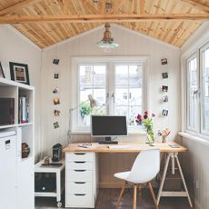 A garden office with a window above and to the side of the desk with built-in drawer storage