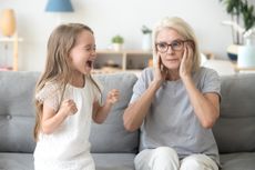 Shocked grandma closing ears not to hear noisy stubborn fussy little granddaughter screaming demanding attention, preschool spoiled kid girl yelling at grandmother, child tantrum manipulation concept