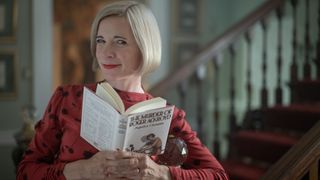 Lucy Worsley in a red dress holds Agatha Christie's novel The Murder of Roger Ackroyd in Agatha Christie: Lucy Worsley on the Mystery Queen