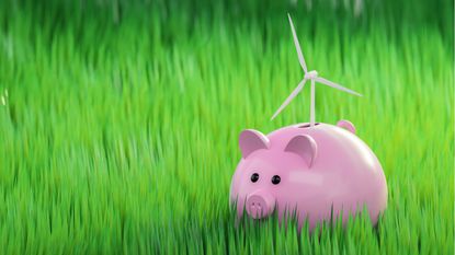 A piggy bank sits in a field of green grass. A tiny wind turbine sits on top.