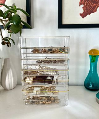 Clear plastic drawer organizers with a gold rim being used to organize small jewelry, stacked up on top of one another