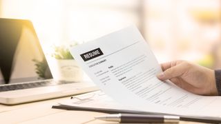 Businessman reviewing his resume on a wooden desk with laptop computer in background