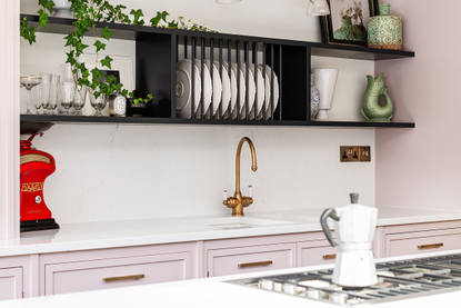 A kitchen with pink cabinetry and black open shelves with open plate rack storage