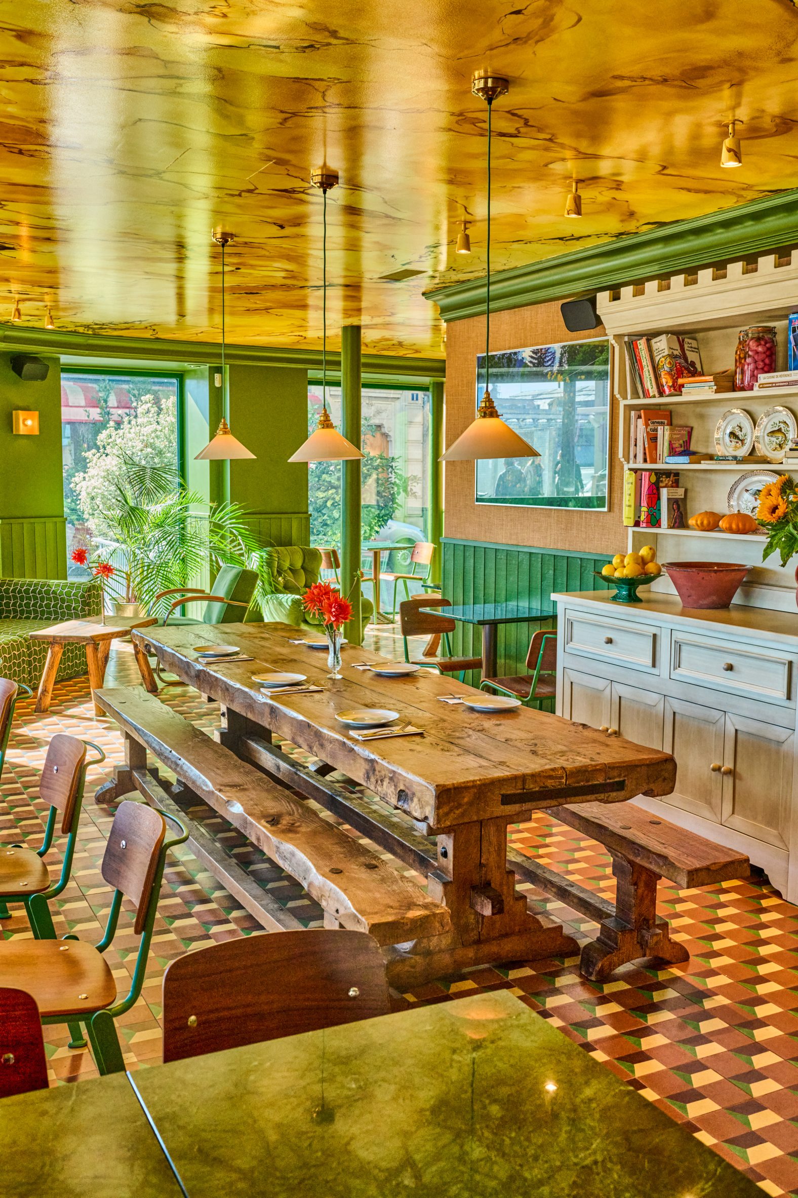 A yellow-tinted dining room decorated in a shabby-chic way, with half wooden walls painted green, lacquered yellow ceilings, checkered tiled floors, wooden furniture, and country touches.