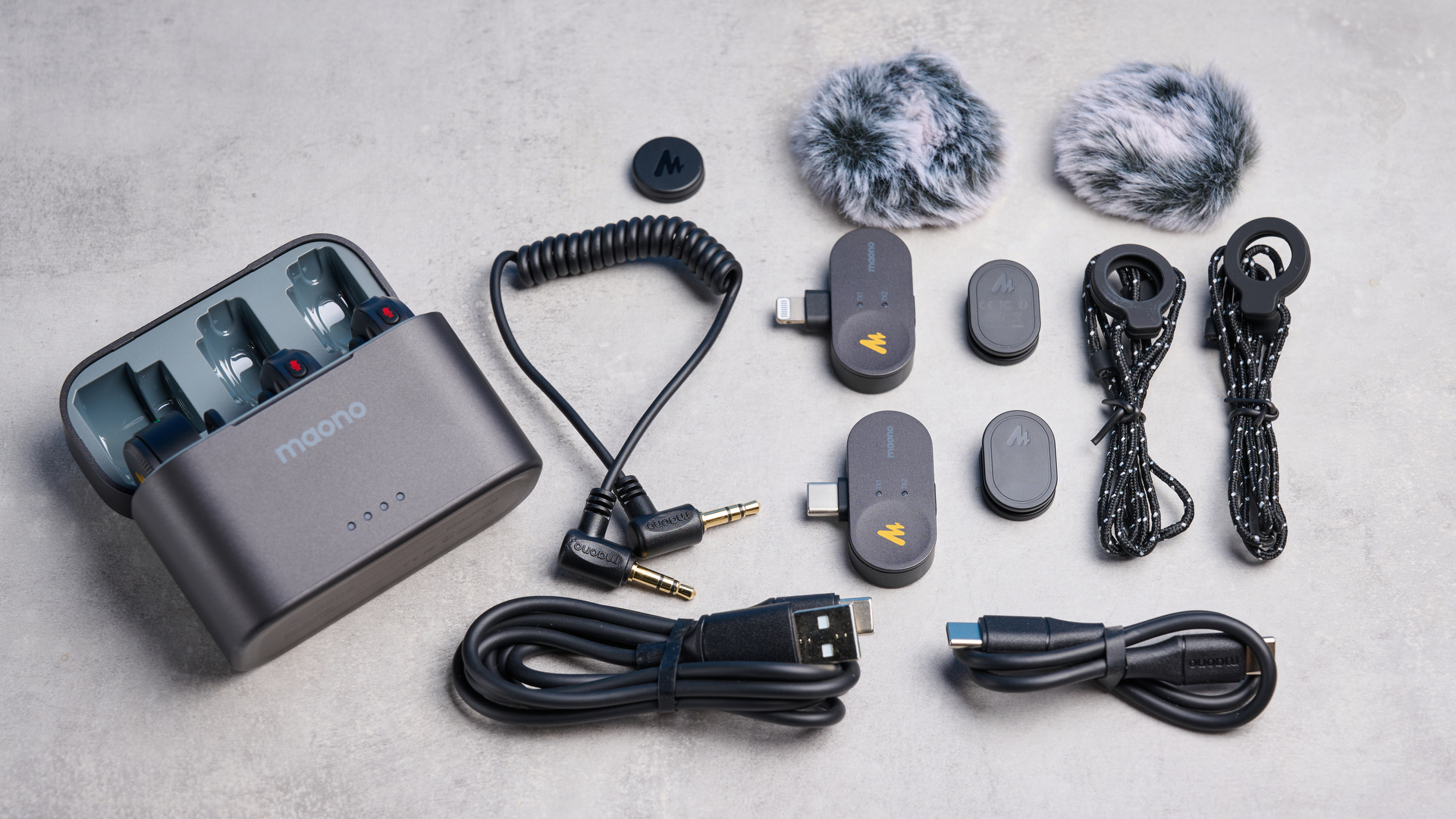 the maono wave t5 lavalier microphone shown against a blue background, showing the transmitters, receivers, and charging case