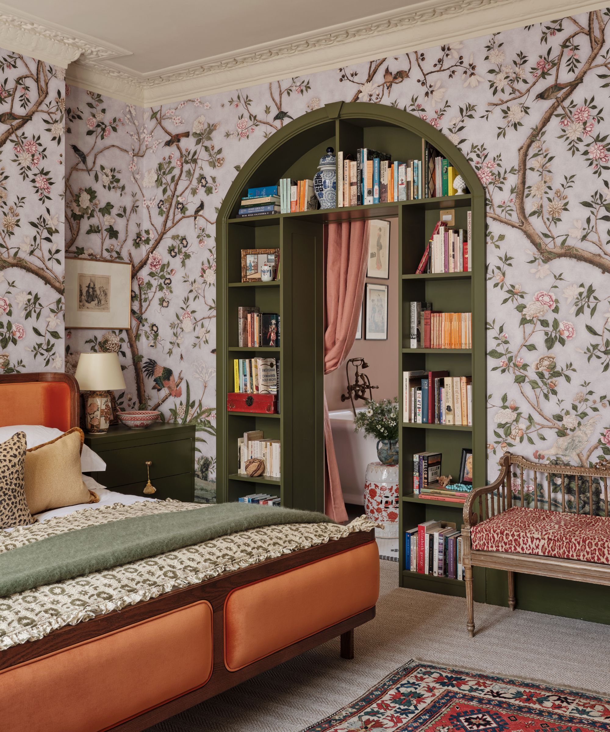 floral mural wallpaper in a bedroom with a door into the utility built with dark green bookcase shelving, a pink drape and an orange bed