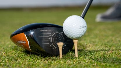 A golf driver lined up with a ball and a tee