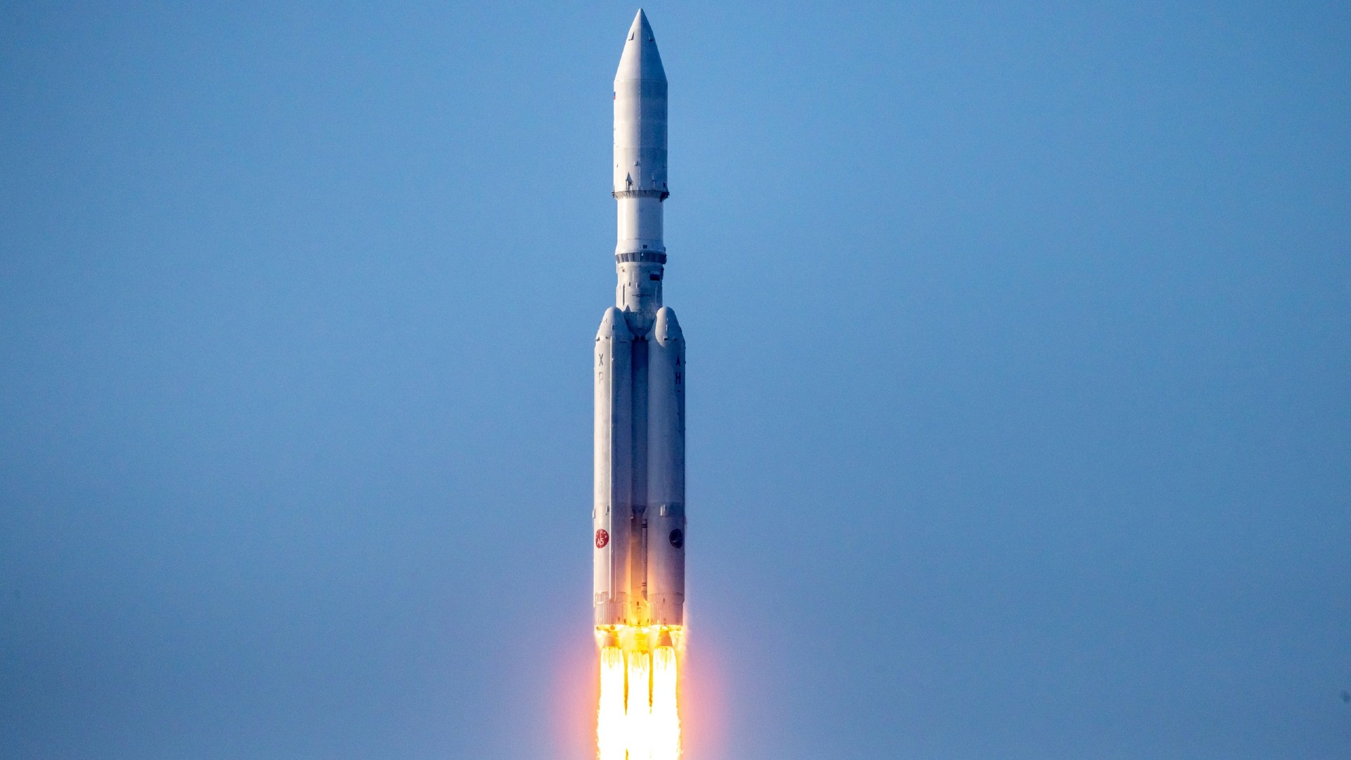 Большая белая ракета с четырьмя маленькими ускорителями взлетает с полосы огня.