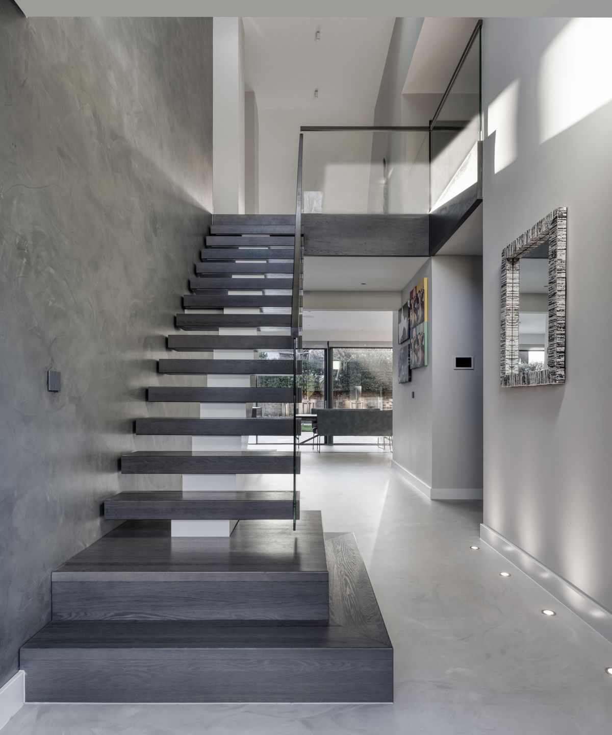 grey floating staircase in double height entrance hall with grey marble walls and floor