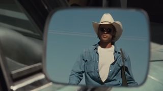 Brad Pitt appears in a car side mirror wearing a cowboy hat and denim