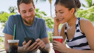 Man and woman sat under palm trees looking at a phone