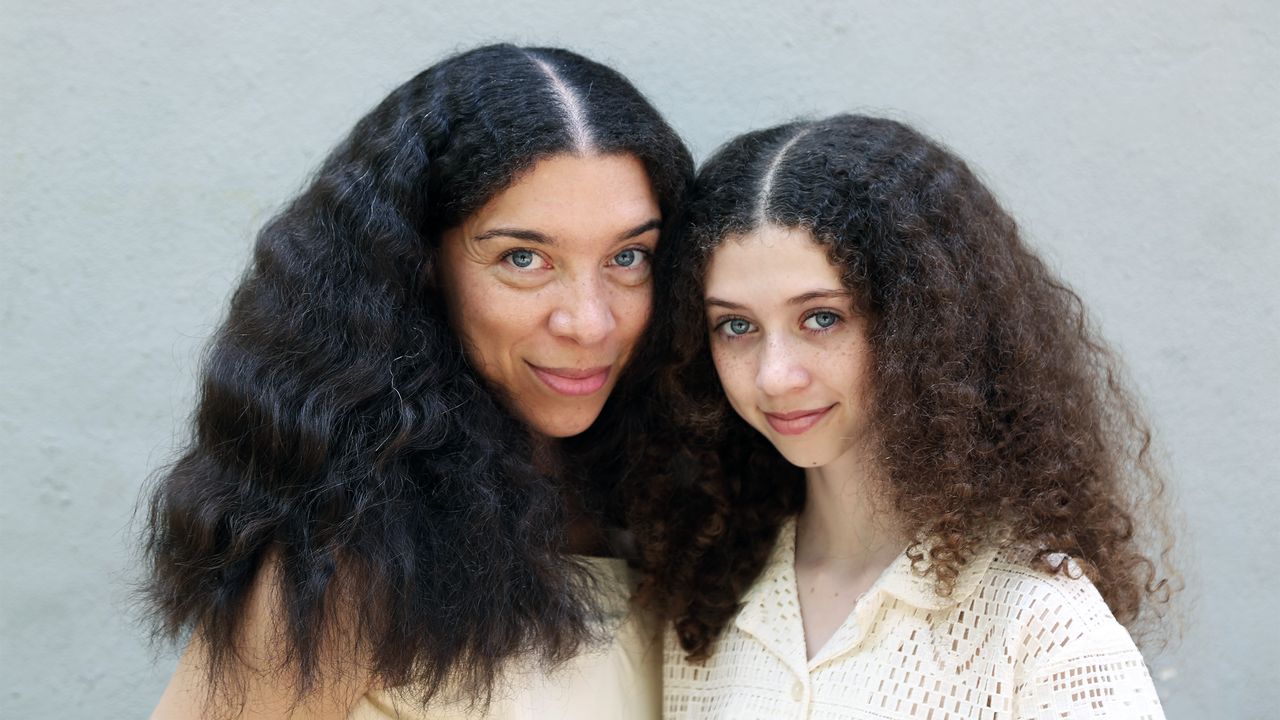 A woman with curly, natural hair next to her daughter, both wearing white tops