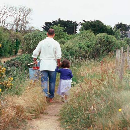 Father holding his young daughter's hand, walking along a path through a garden